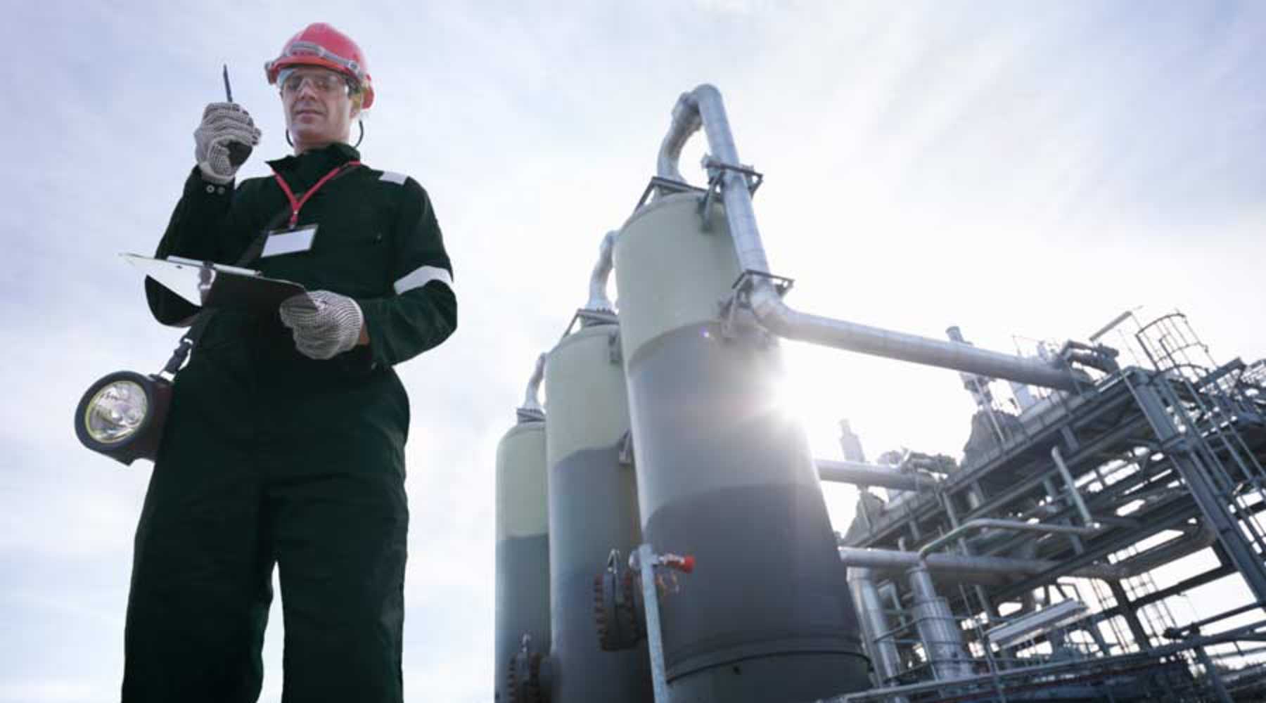 Worker at gas storage plant with walkie talkie and clipboard in hand, sustainability consulting, oil and gas.