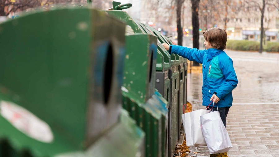 a child disposing of trash in a green recycling bin