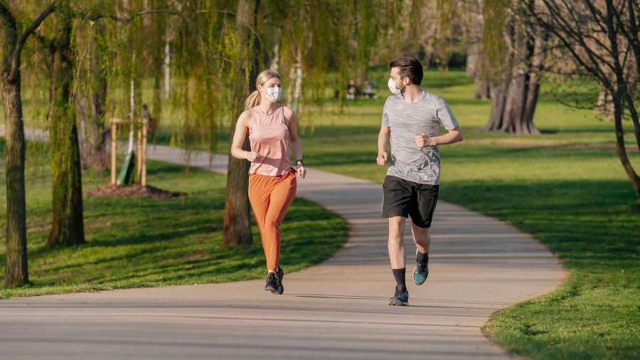 man and woman jogging in the park with their masks on